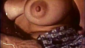 Büyük popolu bir sarışın, klasik bir porno videosunda uzun yanaklı bir adam tarafından göğüsleri ve amcığı yalatılıyor